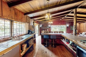 Un intérieur en bois comprenant un coin cuisine, des tabourets de bar et une grande fenêtre.