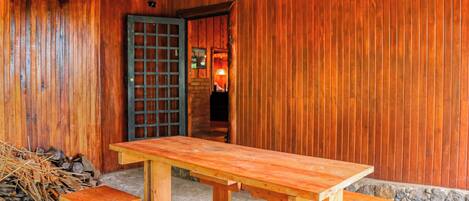 Un interior de madera con una mesa grande, bancos, una puerta y una pila de leña.