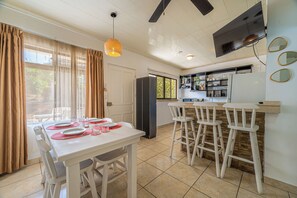 A dining area with a table set for four, a kitchen with a TV, and a bar area with stools. - Playas del Coco Condo w/ Pool: Walk to Beach! (Playas del Coco)