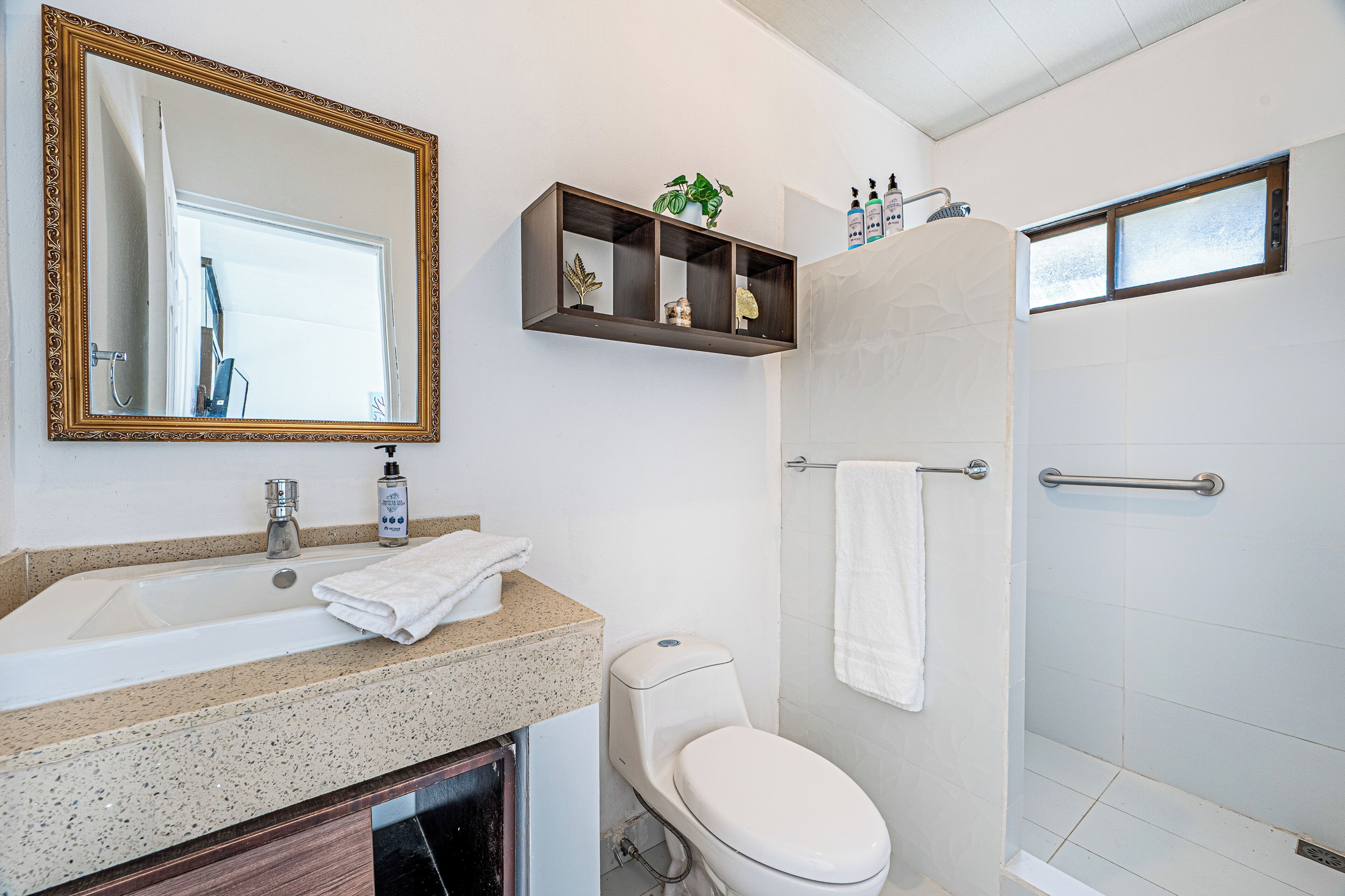 A bathroom with a sink, toilet, shower, and a mirror with an ornate frame.