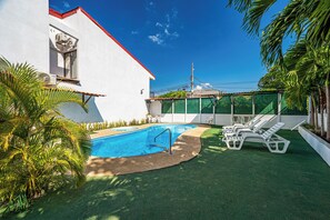 A swimming pool with a surrounding deck, a white building with a red roof, and palm trees. - Playas del Coco Condo w/ Pool: Walk to Beach! (Playas del Coco)