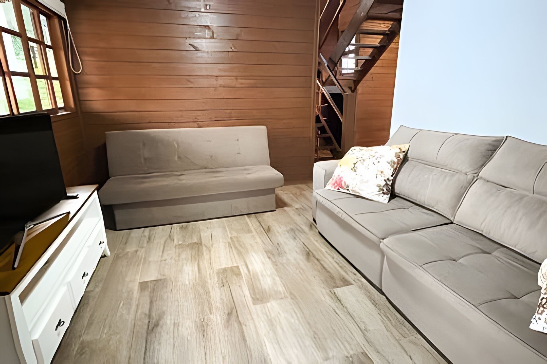 Ein Zimmer mit einer Couch, einem Fernseher und Holzboden.