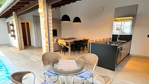 Eine moderne Küche mit einer zentralen Kochinsel, ein Essbereich mit Stühlen und einem Tisch sowie ein Poolbereich mit Liegestühlen.