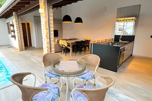 Una cocina moderna con una isla central, un comedor con sillas y una mesa, y una zona de piscina con sillas.
