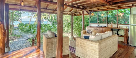 Un espacio de estar al aire libre con techo, mobiliario de mimbre, piso de madera y vista al océano.