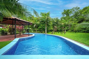 Ein Pool mit Fliesenrand, umgeben von üppiger Vegetation und einer überdachten Sitzgelegenheit.