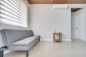 Ein modernes Zimmer mit einer grauen Couch, einem kleinen Holztisch mit Dekoration und einer weißen Tür.