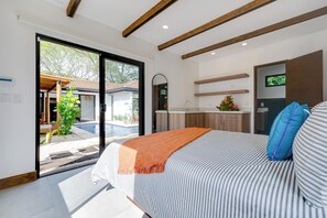 Ein modernes Schlafzimmer mit einem großen Bett, Blick auf einen Swimmingpool und einer Küchenzeile.