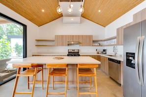 Eine moderne Küche mit einer zentralen Kochinsel, Holzbarhocker und einem Edelstahlkühlschrank.