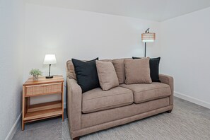 A neutral-colored sofa with a matching side table and a floor lamp in a simple room with white walls and a patterned rug. - Tamarindo Escape: Balcony < 2 Mi to Beach (Tamarindo)