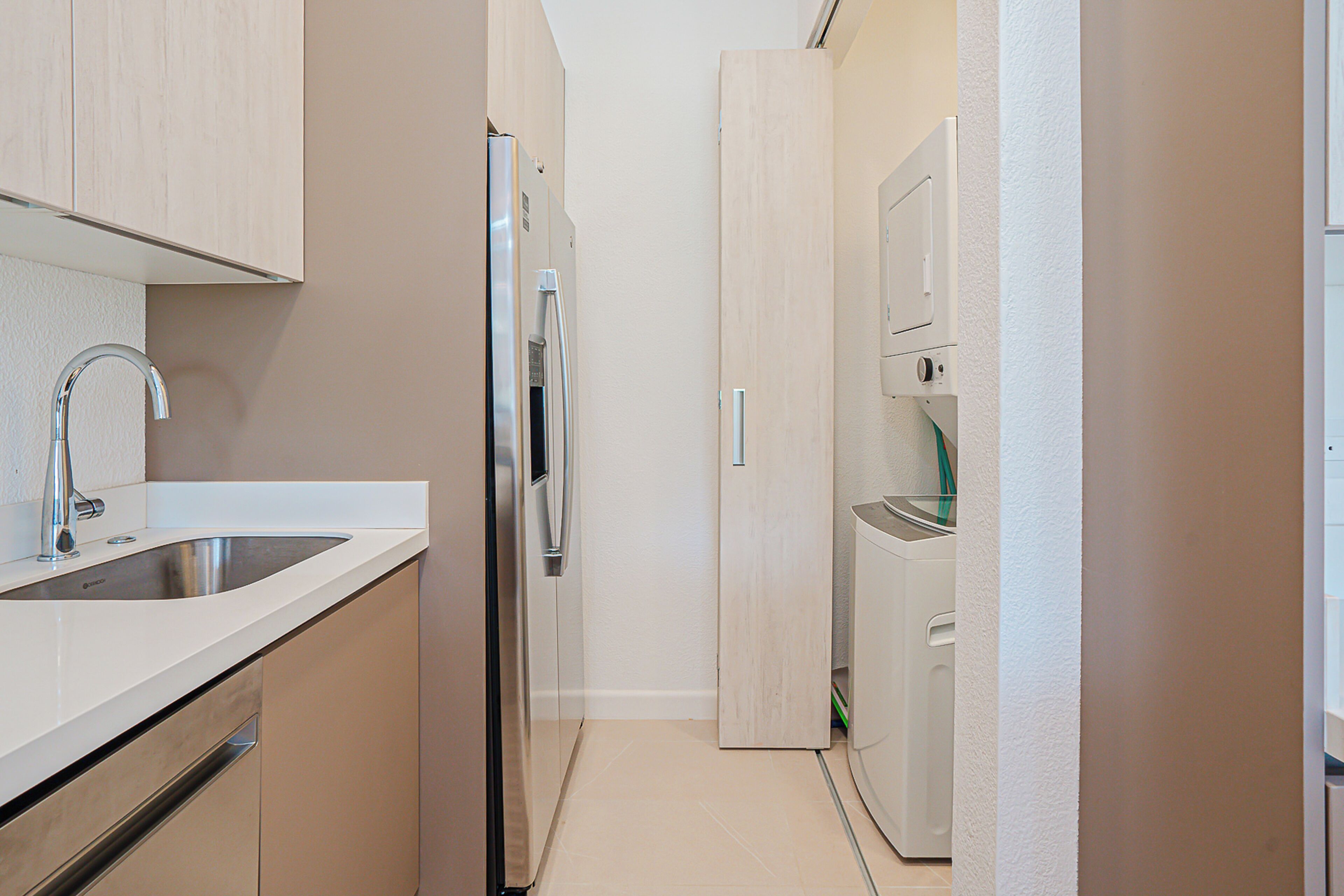 A narrow kitchen with a stainless steel sink, a built-in oven, and a refrigerator.