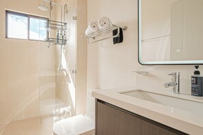 Een moderne badkamer met een douchecabine van glas, een witte wastafel met spiegel en een handdoekrek met twee handdoeken.