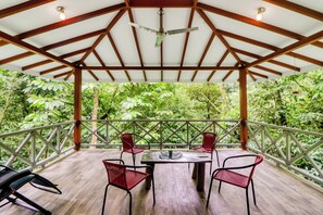 Un espace extérieur aménagé, abrité et doté d’une table et de chaises, entouré d’une végétation luxuriante.