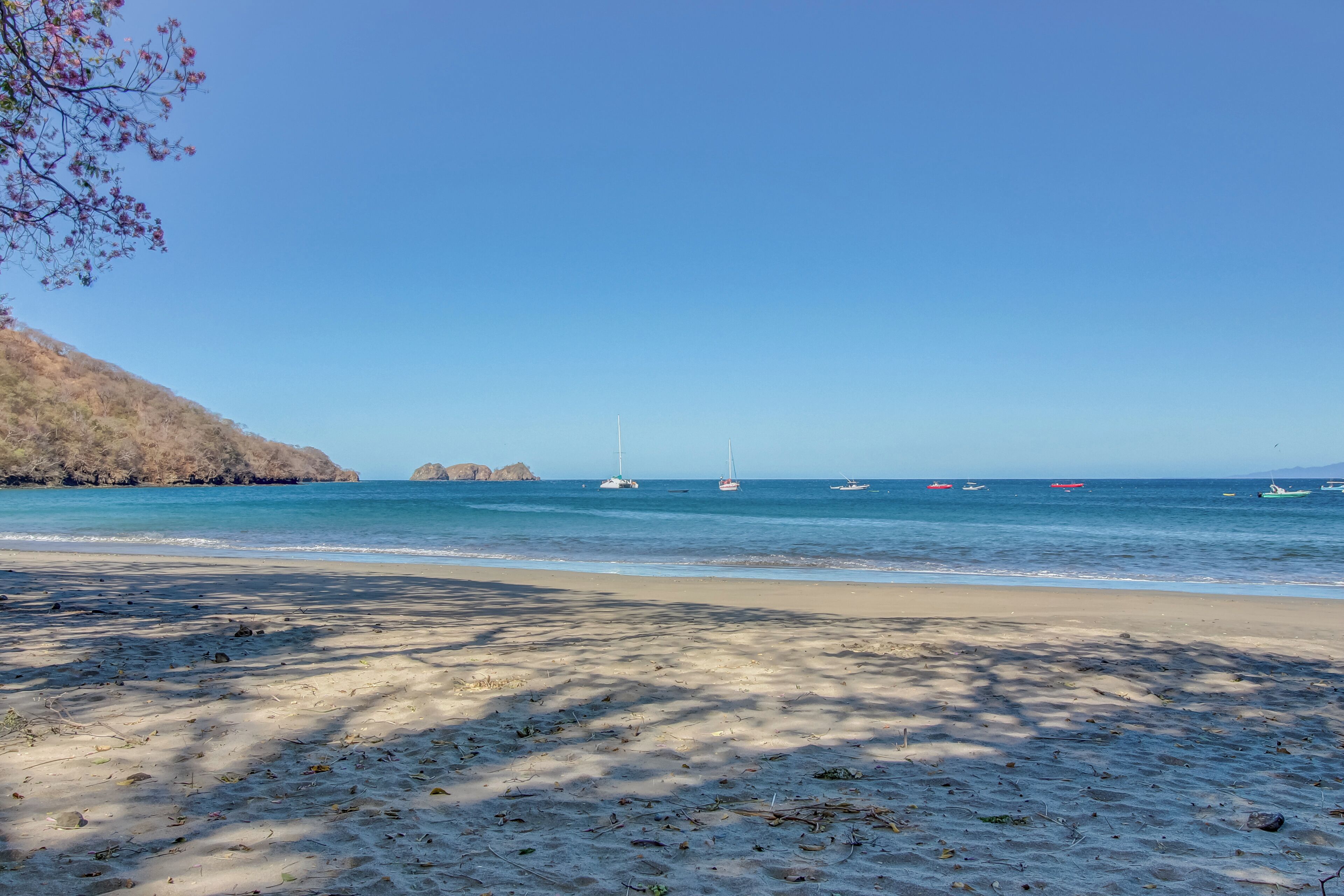 Une plage avec un ciel dégagé, une eau calme et des bateaux.