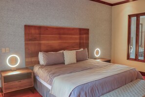A bedroom with a wooden headboard, a bed with multiple pillows, two bedside tables with ring lights, and a window with blinds. - Hacienda Pinilla Villa: Lap Pool, Near Beaches (Tamarindo)