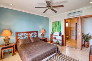 A bedroom with a bed, two bedside tables, a ceiling fan, a wall-mounted TV, and a bathroom visible through an open door. - Stunning 2BR Oceanview 4th-Floor | Balcony (Flamingo Beach)