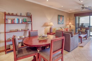 A dining area with a round table and chairs, a bookshelf, a sofa, and a view of the ocean. - Stunning 2BR Oceanview 4th-Floor | Balcony (Flamingo Beach)