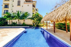A swimming pool with a clear blue water surface, surrounded by a tiled deck and palm trees. - Stunning 2BR Oceanview 4th-Floor | Balcony (Flamingo Beach)