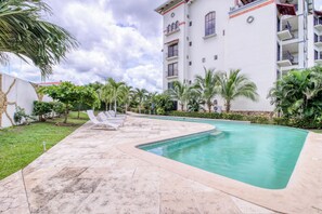 A swimming pool with lounge chairs, surrounded by palm trees and a multi-story building with balconies. - Stunning 2BR Oceanview 4th-Floor | Balcony (Flamingo Beach)