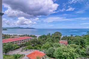 A coastal view with a hotel, lush greenery, and a clear sky. - Stunning 2BR Oceanview 4th-Floor | Balcony (Flamingo Beach)