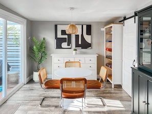 A modern dining area with a white table, brown chairs, and a large abstract wall art piece. - Retro Lounge | Family-friendly, Arcade Games+Patio (San Diego)