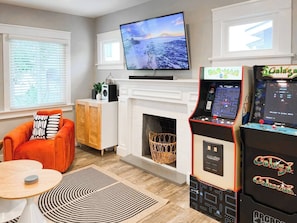 A living room with a flat-screen TV, arcade games, a fireplace, and a cozy seating area. - Retro Lounge | Family-friendly, Arcade Games+Patio (San Diego)