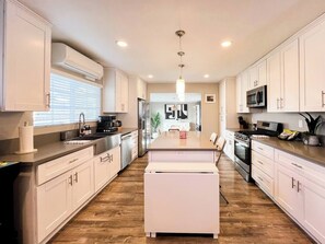 A modern kitchen with white cabinetry, a central island, and a wood floor. - Retro Lounge | Family-friendly, Arcade Games+Patio (San Diego)