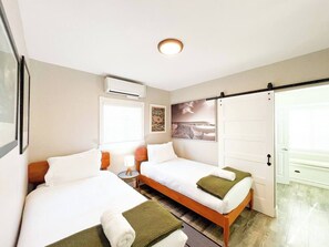 A hotel room with two beds, a small table, an air conditioning unit, and a sliding door. - Retro Lounge | Family-friendly, Arcade Games+Patio (San Diego)