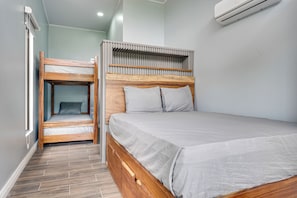 Ein Zimmer mit einem Etagenbett, einem Einzelbett und einem Fenster mit Jalousien.