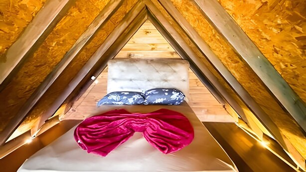 A small, triangular attic bedroom with a bed, pillows, and a red blanket.