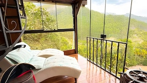 Un dormitorio con cama, piso de madera, ventana con vista a la vegetación y balcón con barandilla.