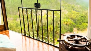 A room with a large window overlooking a lush landscape, a wooden floor, and a vintage-style ship wheel.