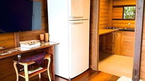 A compact kitchen with wooden walls, a white refrigerator, a small wooden table, and a window with a view of greenery.