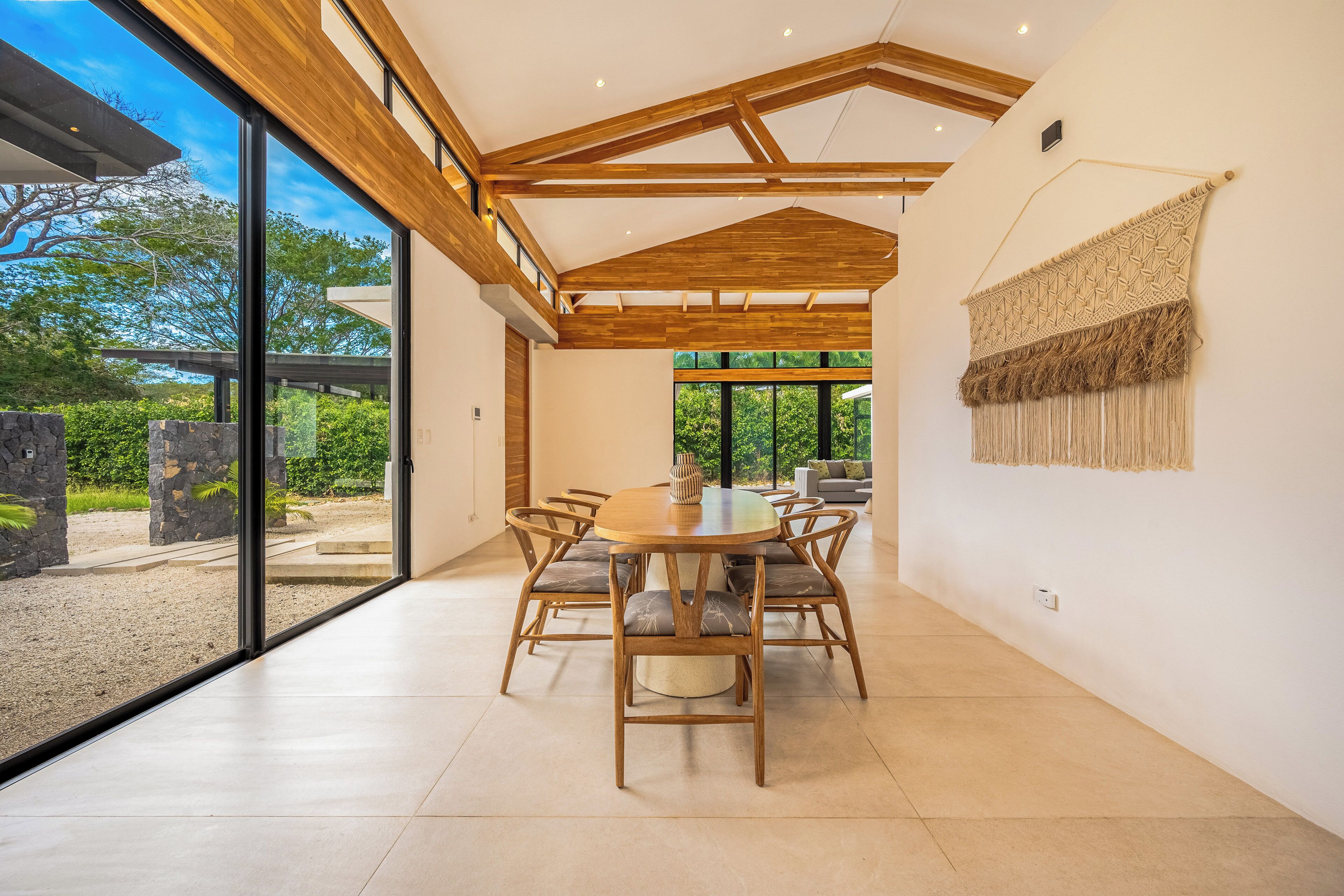 A spacious dining area with a wooden table and chairs, large windows, and a view of greenery outside.