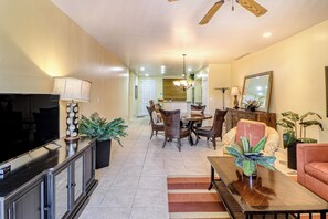 A spacious living area with a television, dining table, and chairs, a kitchen in the background, and a ceiling fan. - Walkable Coco Beach Condo w/ Balcony, Pool (Playas del Coco)