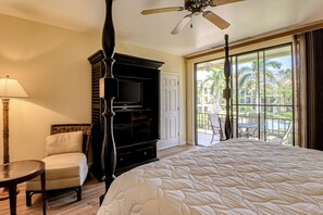 A hotel room with a bed, a television, a chair, a table, a ceiling fan, and a view of the outdoors. - Walkable Coco Beach Condo w/ Balcony, Pool (Playas del Coco)