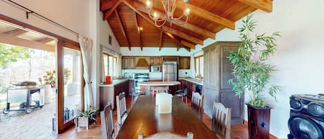 A spacious kitchen with wooden beams, a dining table with chairs, and a large potted plant.