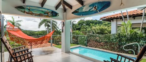 Ein Poolbereich mit einer Hängematte, Schaukelstühlen und Blick auf Pool und Grünflächen.