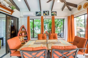 A dining area with a table set for four, surrounded by orange chairs, a decorative centerpiece, and a view of greenery outside. - Villa Sol Resort Gem w/ Soaking Pool & Views! (Playa Hermosa)