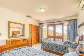 Een slaapkamer met twee bedden, een houten dressoir, een spiegel en een raam met gordijnen.