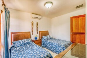Une chambre avec deux lits, une table de chevet, un climatiseur fixé au mur et une porte en bois.