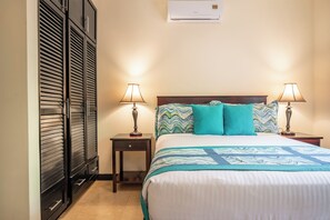 Ein Hotelzimmer mit einem Bett, zwei Nachttischen mit Lampen, einem kleinen Tischchen und einem hölzernen Kopfteil, sowie einer Wand-Klimaanlage.
