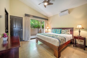 A bedroom with a bed, a nightstand, a lamp, a ceiling fan, and a window with curtains. - Sunny 2BR: Balcony, Pool, Kitchen, Walk to Beach (Playa Ocotal)