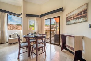 A dining area with a table set for four, a sofa, and a painting on the wall. - Sunny 2BR: Balcony, Pool, Kitchen, Walk to Beach (Playa Ocotal)