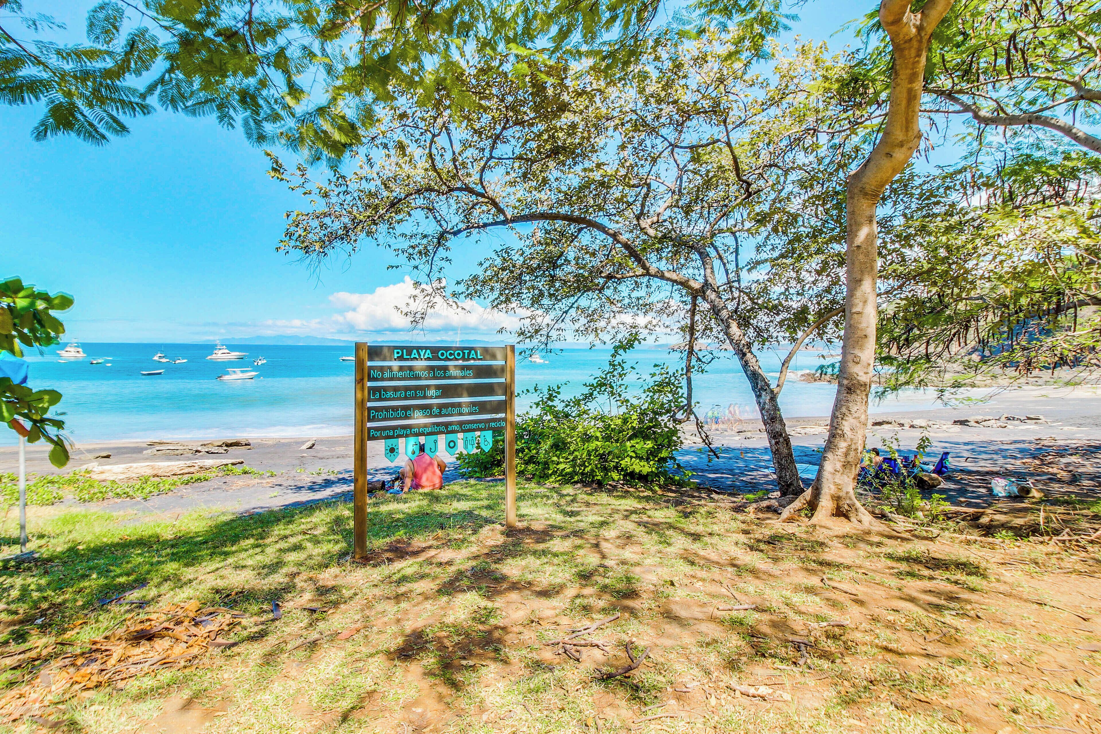 Strandschild mit Umweltrichtlinien und Blick auf das Meer mit Booten.