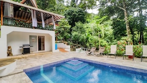 Piscina com borda azulejada, churrasqueira e área externa coberta com espreguiçadeiras.