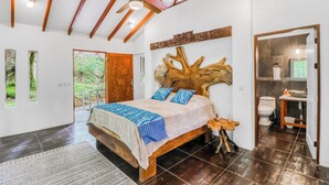 Quarto com cama grande, ventilador de teto, cabeceira de madeira e vista para o exterior através de uma porta.