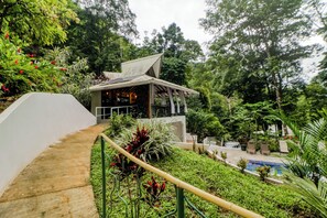 Un bâtiment moderne doté d’un toit en pente, entouré d’une végétation luxuriante et comprenant un espace piscine.