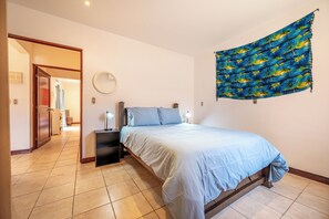 A bedroom with a bed, bedside lamps, a wall-mounted mirror, and a door leading to another room. - 3 Mi to Tamarindo & Beach: Cozy 2BR Home (Tamarindo)
