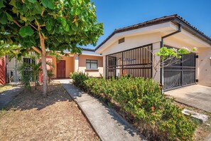 A residential building with a paved driveway, a gated entrance, and a small garden area with shrubs and a tree. - 3 Mi to Tamarindo & Beach: Cozy 2BR Home (Tamarindo)